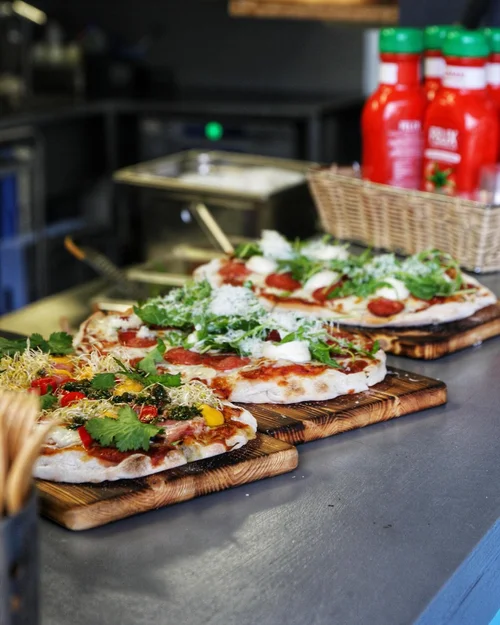Lähikuva puulautasille katetuista artesaanipizzoista, jotka on koristeltu runsailla tuoreilla yrteillä ja vihanneksilla.