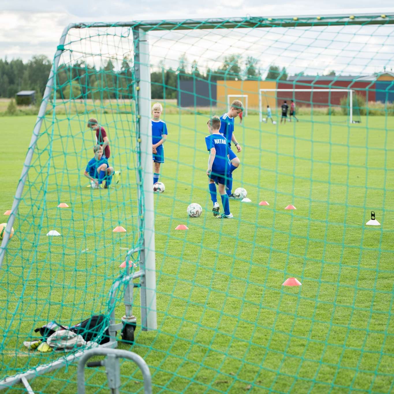 Lapset harjoittelevat jalkapalloa kent&auml;ll&auml; valmentajan ohjauksessa.