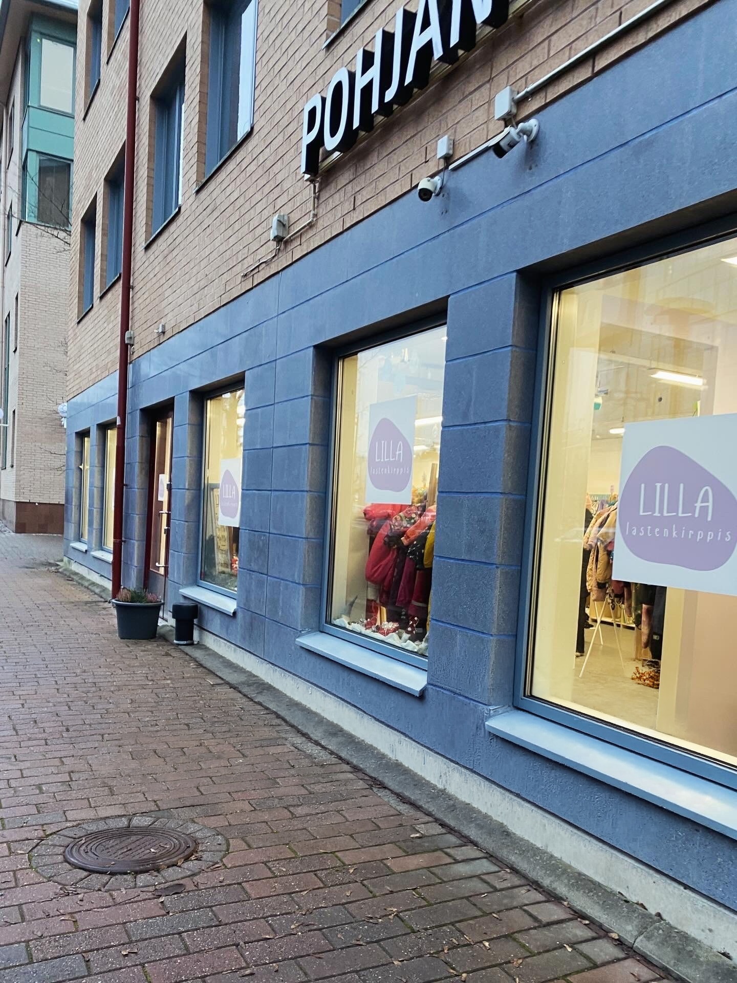 Rakennuksen katutasossa n&auml;kyy liiketila, jonka ikkunoissa on tekstit &ldquo;LILLA lastenkirppis&rdquo;. Ikkunoiden l&auml;pi n&auml;kyy lastenvaatteita rekiss&auml; ja esille aseteltuna. Rakennuksen sein&auml; on alaosasta sininen ja yl&auml;osasta tiiliverhoiltu. Yl&auml;puolella on osittain n&auml;kyv&auml; kyltti &ldquo;POHJAN&hellip;&rdquo;. Kuvassa on my&ouml;s kapea mukulakivinen k&auml;velytie rakennuksen vieress&auml;.